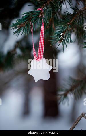 Hausgemachte kleine Weihnachtssterne aus Eis, das an einem schneebedeckten Tannenzweig an einem rot-weißen karierten Band hängt Stockfoto