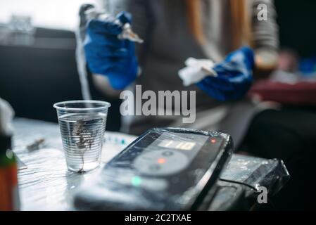 Weibliche Tätowierer Händen in Blau sterile Handschuhe hält Tattoo Maschine, professionelle Arbeitsmittel für den Hintergrund. Tattooing in Salon Stockfoto