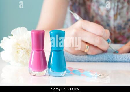 Im Vordergrund befinden sich zwei Nagellacke (ein rosa und ein blau) mit Maniküre-Werkzeugen. Im Hintergrund aus dem Fokus, Frauen Hände malen sie Stockfoto