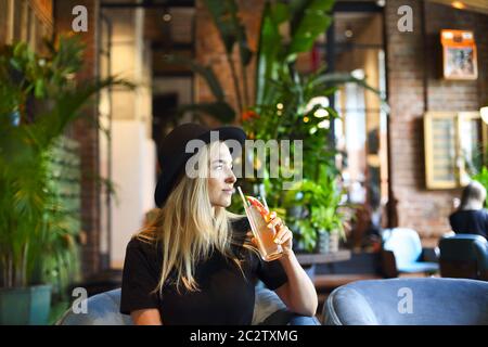 Attraktive niedliche kaukasische Mädchen in schwarzem T-Shirt und schwarzen Hut trinkig kalten Zitrusfrüchten Saft oder Limonade Stockfoto