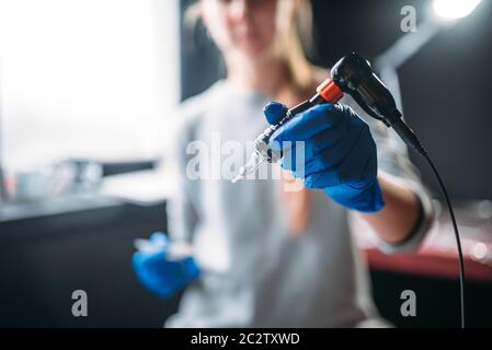 Weibliche Tätowierer in Blau sterile Handschuhe hält Tattoo Maschine in der Hand, professionelle Tätowierer tools. Tattooing in Salon Stockfoto