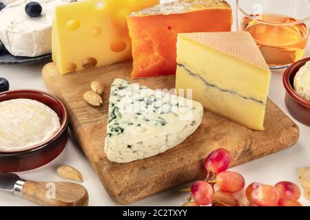 Käseplatte. Blue Cheese, Red Leicester, Brie, Emmentaler und andere mit Wein und Trauben auf weißem Hintergrund Stockfoto