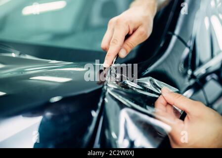 Arbeiter Hände installiert Auto lack Schutzfolie auf der Motorhaube. Transparente Schutzschicht vor Kratzern und Schrammen Stockfoto