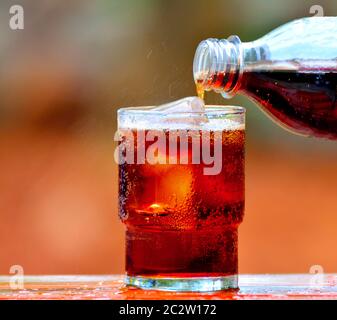 Gießen von Cola in ein Glas Eis auf unscharfen Hintergrund. Stockfoto