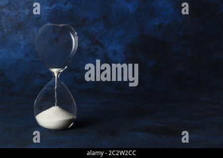 Die Zeit läuft. Eine Sanduhr mit Sand durch fallende, auf dunkelblauem Hintergrund mit Kopie Raum Stockfoto