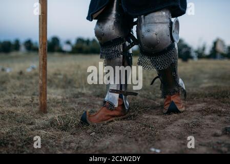 Mittelalterliche Ritterbeine in Metallpanzerung, Rückansicht, großes Turnier. Gepanzerte alte Krieger in Rüstung posiert auf dem Feld Stockfoto