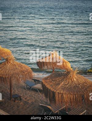 Leere Strandliegen am Strand in der Nähe des Meeres. Ein ruhiger Ort zum Entspannen unter Strohschirmen. Leere Strandliegen Stockfoto