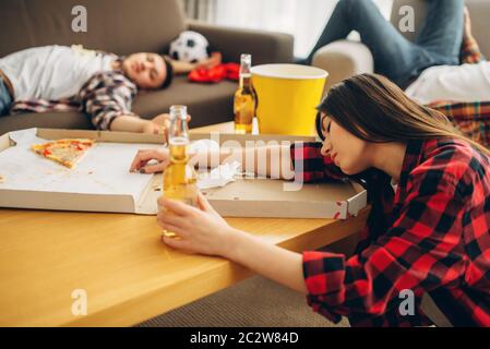 Fußball-Fans zu Hause schlafen, Kater morgen. Betrunkene Freunde nach der Feier des Sieges der Lieblingsmannschaft, Party mit Bier, Pizza und Popcorn Stockfoto