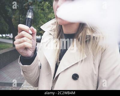 Blonde Mädchen in beige Trenchcoat Verdampfung Obst e-Flüssigkeit mit sehr beliebten Vaporizer Gerät Stockfoto