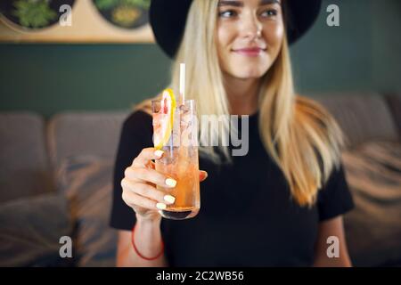 Attraktive niedliche kaukasische Mädchen in schwarzem T-Shirt und schwarzen Hut trinkig kalten Zitrusfrüchten Saft oder Limonade Stockfoto