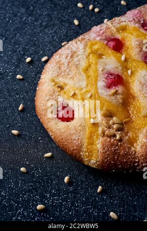 Nahaufnahme eines Coca de Sant Joan, ein typischer süßer flacher Kuchen aus Katalonien, Spanien, gegessen an der St. Johns Eve, auf einer schwarzen Stoffoberfläche mit pi bestreut Stockfoto