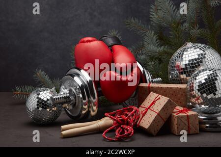 Sportausrüstung: Kurzhantel, Boxhandschuhe, Springseil, Tannenzweig, Weihnachtsschmuck, Geschenke auf dunkelgrauem Hintergrund. Fitness, Sport, gesundes Leben Stockfoto