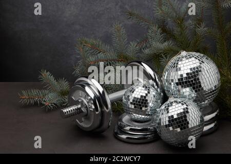 Sportgeräte (Hantel mit Gewichten), Tannenzweig, Weihnachtsschmuck auf dunkelgrauem Hintergrund. Fitness, Sport oder gesundes Lifestyle-Konzept. Neu Stockfoto