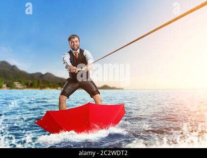 Glücklich Kaufmann auf dem Wasser Surfen im roten Regenschirm Stockfoto