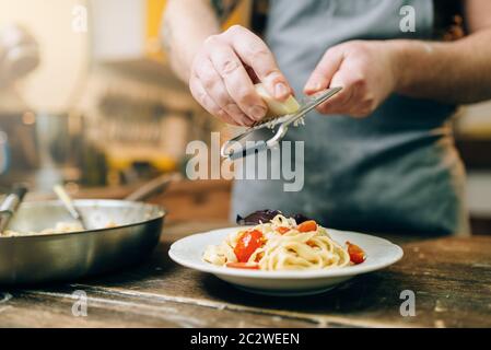 Männliche chef Roste Käse in der Platte mit frisch gekochten Nudeln, Pan auf hölzernen Küchentisch. Hausgemachte Bandnudeln Vorbereitung. Traditionelle ita Stockfoto