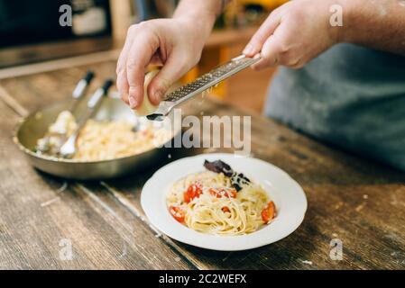 Männliche chef Hände Roste Käse in der Platte mit frisch gekochten Bandnudeln, Pan auf hölzernen Küchentisch. Hausgemachte Pasta Vorbereitung. Tradition Stockfoto