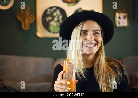 Attraktive niedliche kaukasische Mädchen in schwarzem T-Shirt und schwarzen Hut trinkig kalten Zitrusfrüchten Saft oder Limonade Stockfoto