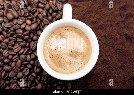 Eine Tasse frischen Kaffee mit Schaum. Hintergrund von Kaffeebohnen und gemahlenem Kaffee. Stockfoto