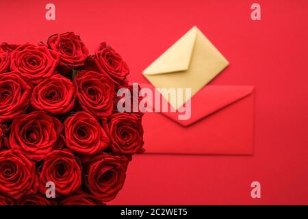 Liebesbrief und Blumenlieferservice am Valentinstag, luxuriöser Strauß roter Rosen und Kartenumschläge auf rotem Hintergrund Stockfoto