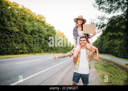 Junges Anhalter-Paar mit leerem Karton. Anhalter Abenteuer von Mann und Frau. Glückliche Anhalter auf der Straße Stockfoto