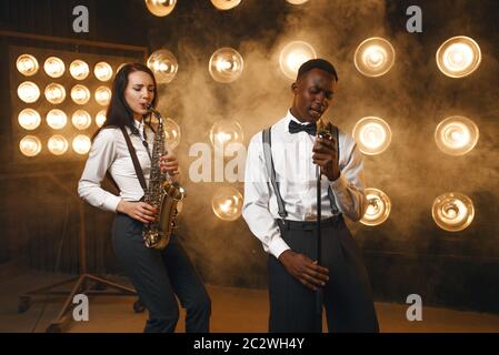 Männlicher Jazzmann und Saxophonistin mit Saxophon auf der Bühne mit Spotlights. Jazzkünstler spielen auf der Bühne Stockfoto