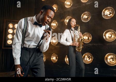 Männlicher Jazzmann und Saxophonistin mit Saxophon auf der Bühne mit Spotlights. Jazzkünstler spielen auf der Bühne Stockfoto