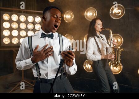 Männlicher Jazzmann und Saxophonistin mit Saxophon auf der Bühne mit Spotlights. Jazzkünstler spielen auf der Bühne Stockfoto