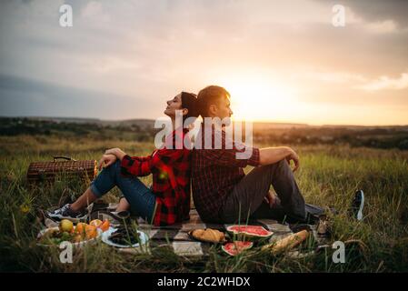 Liebe Paar mit dem Rücken zueinander sitzen auf den Sonnenuntergang, Picknick im Feld. Romantischen Quark auf Sonnenuntergang, Mann und Frau im Freien Abendessen, glücklich Stockfoto