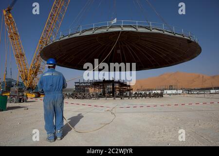 Ein Besatzungsmitglied hält ein Seil, um den schweren Hub eines großen Deckels zu steuern, der während des Baus einer neuen Ölanlage in der Sahara an der Oberseite eines Druckbehälters angebracht wird. Stockfoto