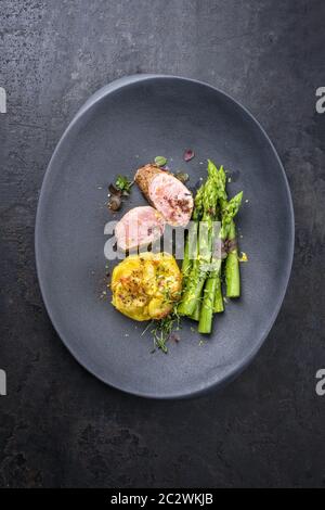 Gebratenes iberisches Schweinefilet in Scheiben geschnitten mit blanchierten grünen Spargel und Kartoffelgratin Dauphinois mit Gewürzen als Draufsicht auf einem Cast iro Stockfoto