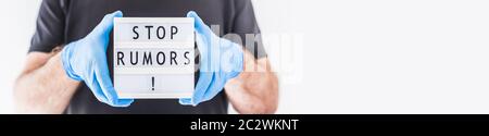 Fake News Infosemics during Covid-19 Pandemie Concept. Mann trägt Schutzmaske und medizinische Handschuhe an den Händen halten Leuchtkasten mit Text Stop Rumors. Stockfoto
