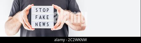 Fake News Infosemics during Covid-19 Pandemie Concept. Mann Hände halten Leuchtkasten mit Text Stoppen Fake News im Vordergrund. Die Leute wollen den Trut kennen Stockfoto