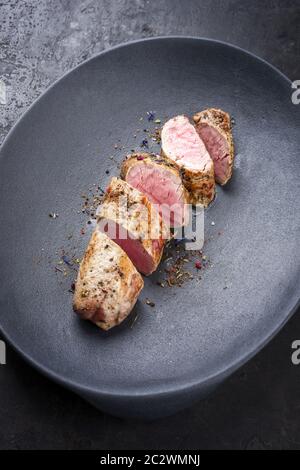 Gebratenes iberisches Schweinefilet in Scheiben geschnitten mit Gewürzen als Nahaufnahme in einer Gusseisen-Design-Platte Stockfoto