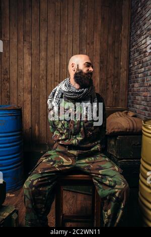 Captive Soldat sitzt auf einem Stuhl, Schrecken des Krieges gebunden. Terrorismus und Terror, militärischen Mann in khaki Camouflage, Barrel Kraftstoff oder Chemikalien auf Backgr Stockfoto