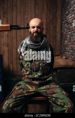 Captive Soldat sitzt auf einem Stuhl gebunden, Pistole zeigte auf seinen Kopf, den Schrecken des Krieges. Terrorismus und Terror, militärischen Mann in khaki Camouflage auf interrogati Stockfoto