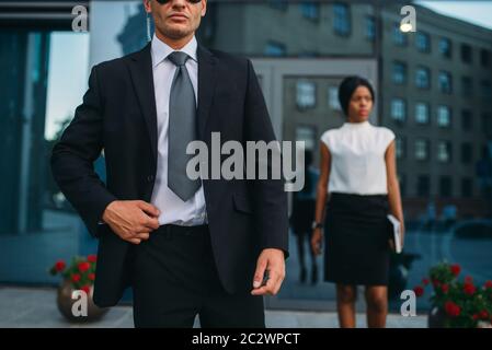 Leibwächter in Anzug und Sonnenbrille, weiblich VIP-Kunde für den Hintergrund. Security Guard ist eine riskante Beruf, professionelle Bewachung, business Personen Protein Stockfoto