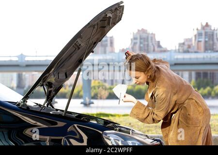 Selbstbewusste kaukasische Frau Fahrer Überprüfung Ölstand im Auto Motor Messstab, Stadtbild auf Hintergrund. Stockfoto