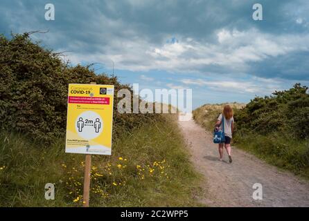 County Kerry, Irland - Frau, die zum Strand an der Westküste der Grafschaft Kerry, Covid-19 soziale Distanzierung Zeichen am Eingang Stockfoto