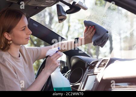 Nahaufnahme der Frau Fahrer Reinigung Auto Windschutzscheibe mit Spray, Wischtücher mit Mikrofaser von Staub und Schmutz. Stockfoto