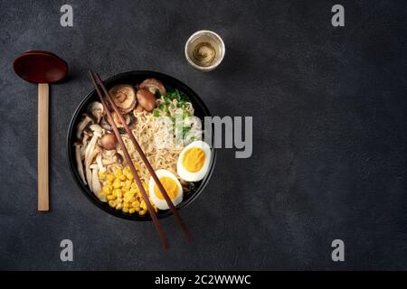 Ramen. Soba Nudeln mit Ei, Shiitake und Enoki-Pilzen, Mais und Schalotten, von oben auf dunklem Grund mit c geschossen Stockfoto