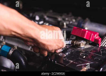 Hand des Techniker Service überprüfen Sie die Batteriespannung und schalten Sie die Batterie Schraube lose in einer Garage. Stockfoto