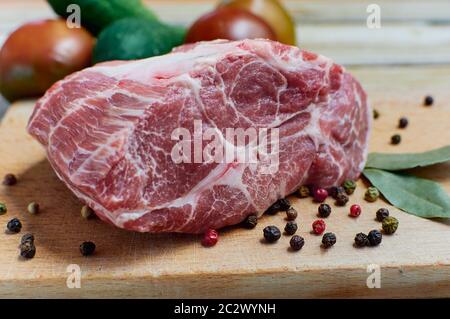 Rohes Fleisch mit Gewürzen in einem Holzbrett. Frisches Gemüse im Hintergrund Stockfoto