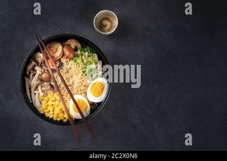 Ramen. Soba Nudelsuppe mit Ei, Shiitake und Enoki-Pilzen, Mais und Frühlingszwiebeln, von oben auf dunklem Hintergrund w Stockfoto