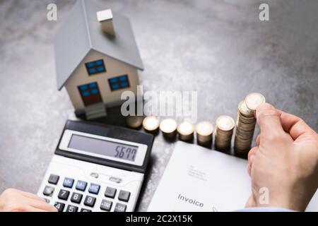 Geschäftsmann mit Münzen und Haus Modell mit Taschenrechner Stockfoto