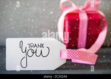 Englisch Kalligraphie Danke. Rosa vorhanden, die mit Bogen und Schild. Grauer Beton Hintergrund und Schneeflocken Stockfoto