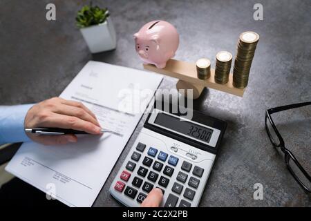Mann Berechnet Bill Near Pink Piggybank Und Erhöht Gestapelte Münzen Balancing Auf Seesaw Stockfoto