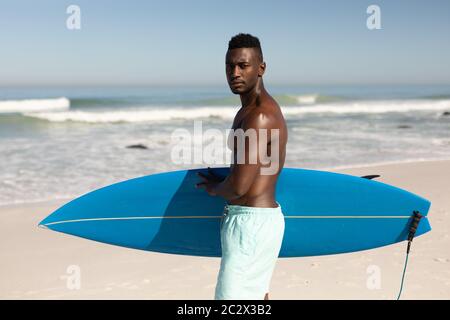 Afroamerikanischer Mann mit Surfbrett am Strand Stockfoto