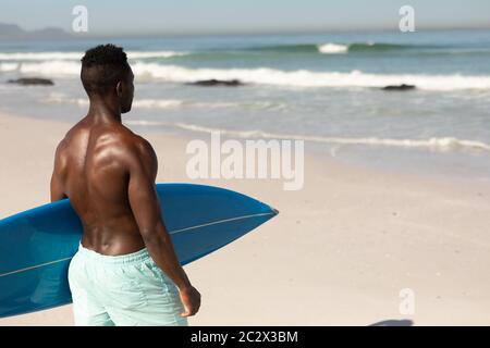 Afroamerikanischer Mann mit Surfbrett am Strand Stockfoto