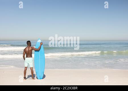 Afroamerikanischer Mann mit Surfbrett am Strand Stockfoto