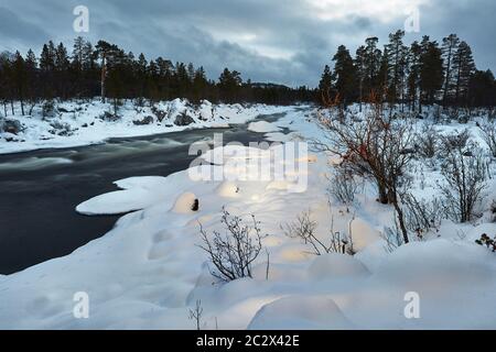 Schneller Fluss fließt im nordischen Winter Stockfoto